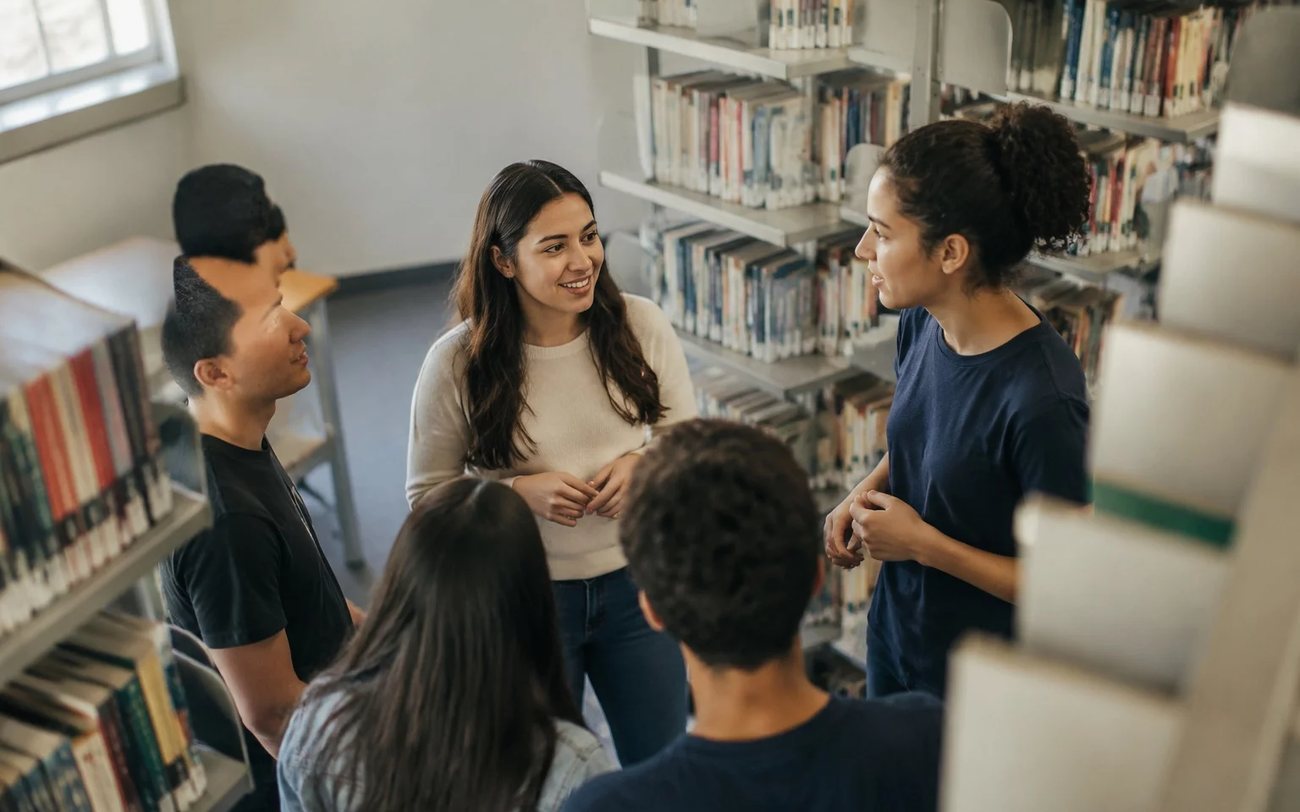Grupo de pé entre prateleiras de livros, conversando sobre um tema de debate